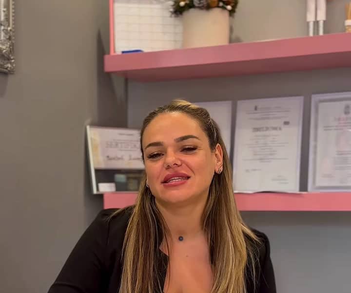 Irma za stolom u studiju, ispred ružičastih polica sa sertifikatima